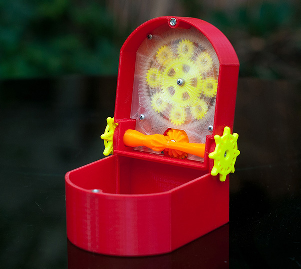 open mechanical box in red, yellow, and orange, showing gears attached to the underside of the lid