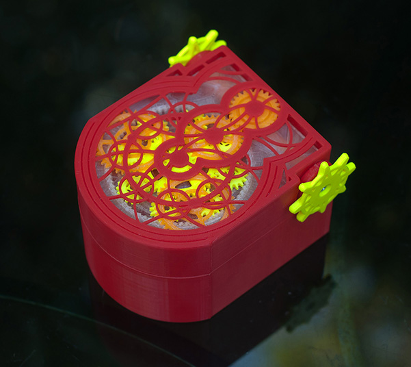 closed mechanical box in red, yellow, and orange, showing gears through the holes in the lid